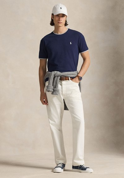 Tumesinine t-särk valge äärega, valged teksad, hall kampsun, mis on vöökoha juures seotud, ning valged tossud tumesiniste detailidega. Valge nokamüts.