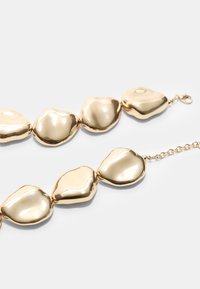 Collana in tono oro con anelli in metallo di forma irregolare, lucidi e con una texture liscia, chiusura a gancio.