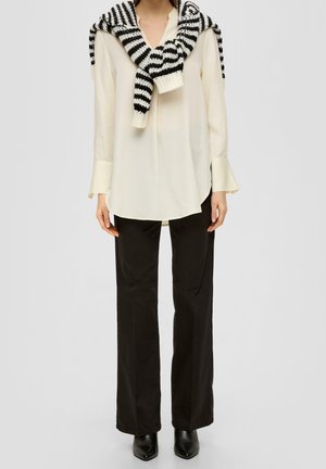 Blusa crema clara con cuello redondo y puños acampanados; combinada con pantalones anchos negros. Una bufanda de punto a rayas blancas y negras está colocada sobre ella.