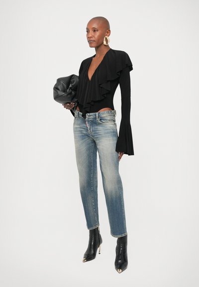 Μαύρο κορμάκι με μακριά μανίκια και βολάν στο μπροστινό μέρος, συνδυασμένο με ανοιχτό μπλε τζιν παντελόνι με ίσια γραμμή και μαύρα μποτάκια μέχρι τον αστράγαλο με χρυσές λεπτομέρειες.