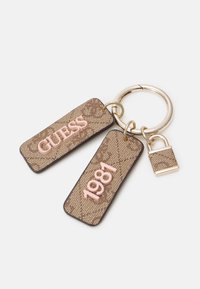 Porte-clés avec deux étiquettes texturées marron affichant "GUESS" et "1981" en texte rose, et un petit charmant cadenas assorti sur un anneau doré.
