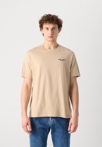 Beige bomulds t-shirt med korte ærmer, rund halsudskæring og sort tekst "Marc O'Polo Denim" på venstre bryst. Standard pasform.