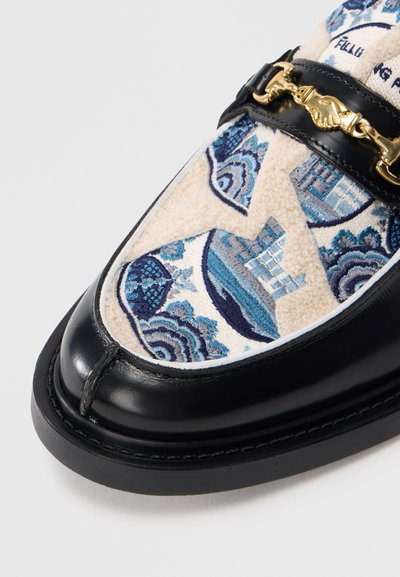 Μαύρο δερμάτινο μοκασίνι με κεντητό υλικό σε μπλε και κρεμ σχέδια, με δι ακοσμητική χρυσή αλυσίδα στο πάνω μέρος.