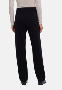 Zwarte broek met wijde pijpen en een zachte textuur, voorzien van een elastische tailleband, ontworpen voor comfort. Geen zichtbare patronen, gecombineerd met platte schoenen.