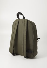 Mochila de color verde oliva hecha de tela duradera, con correas acolchadas, un asa en la parte superior y esquinas redondeadas y elegantes para un diseño aerodinámico.