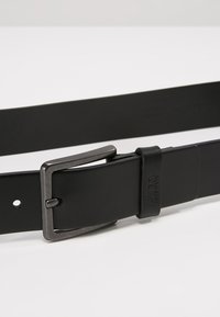 Curea din piele neagră cu finisaj mat, dotată cu o cataramă din metal de culoare argintie și găuri ajustabile pe curea pentru personalizarea dimensiunii.