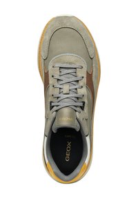Sneaker grigia con tomaia in mesh e suede, dettagli marroni, lacci tondi e un tab sul tallone giallo. La suola è bianca con dettagli testurizzati.
