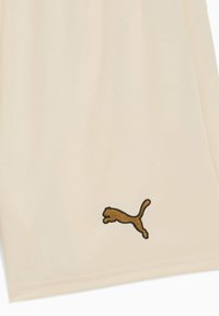Bermudas deportivas beige hechas de una tela ligera, con un logo bordado marrón de Puma en la pierna izquierda. Textura limpia y suave.
