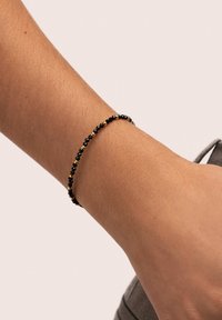 Pulsera de cuentas negras y doradas en una muñeca, con un diseño delicado que alterna pequeñas cuentas negras con detalles dorados.