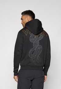 Black hoodie with a graphic design of a snake and "VENOM" text in orange. Features a drawstring hood and ribbed cuffs and hem.
