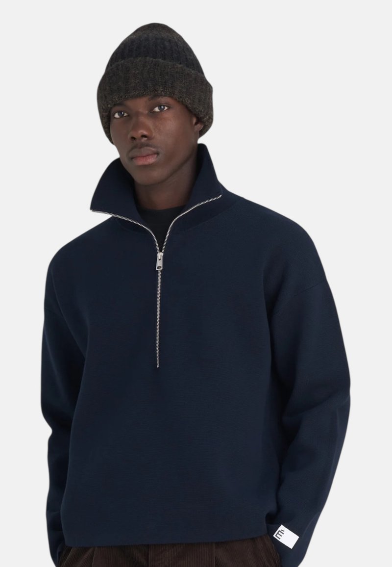 Pull zip en coton marine avec un col montant, tissu texturé et détail en zip argenté. Assorti à un bonnet en tricot sombre.