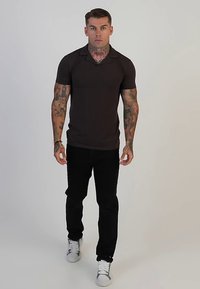 Musta, lyhythihainen poolopaita, jossa on kaulus ja slim fit -istuvuus, yhdistettynä mustiin housuihin ja valkoisiin lenkkareihin, mallin yllä neutraalilla taustalla.