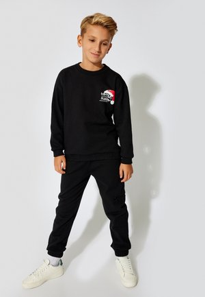 Sort sweatshirt med teksten "WINTER SEASON" i rød og hvid på brystet, parret med matchende sorte sweatpants og hvide sneakers.
