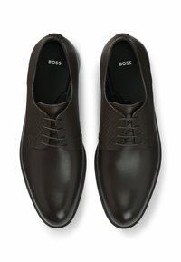 Scarpe in pelle marrone con una tomaia testurizzata e decorata, punta liscia e suola piatta. Presentano lacci e un marchio sulla soletta.