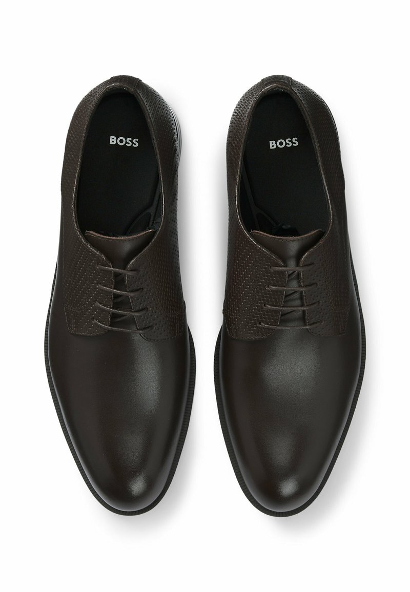 Des chaussures en cuir marron avec un dessus texturé et motif, un bout lisse et une semelle plate. Comprend des lacets et un logo sur la semelle intérieure.