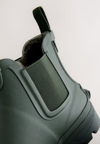 Gros plan d'une botte cheville vert foncé avec panneau latéral élastique, languette de tirage et doublure intérieure douce.