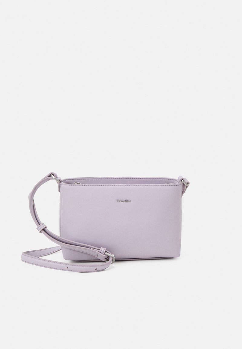 Pieni purppuranvärinen nahkainen olkalaukku, jossa on suorakulmainen muoto, vetoketjukiinnitys ja irrotettava hihna. Sileä pinta ja minimalistinen muotoilu.