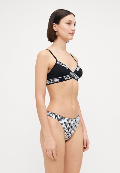 Black bikini with thin straps, featuring white "Moschino" logo band. Bottoms are black and white with prominent letter patterns. Smooth texture.