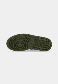 Semelle de basket Nike vert foncé avec motifs circulaires et quadrillés et logo Nike au centre sur un fond clair uni.