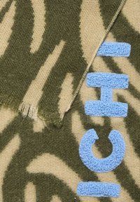 Sciarpa lavorata a maglia con un motivo camouflage in verde oliva e beige, con testo ricamato blu e bordi sfilacciati per un tocco di texture.