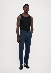 Black sleeveless tank top, dark blue jeans, and black shoes. The outfit features a fitted design with a classic cut and standard finishes.
