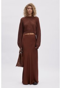 Brun cropped strikkegenser med løs vev, kombinert med en lang brun satengskjørt og en brun skinnveske.