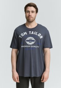 Czarna bawełniana koszulka z krótkim rękawem. Zawiera białe i niebieskie napisy, w tym "TOM TAILOR" i "PREMIUM QUALITY". Luźny krój.