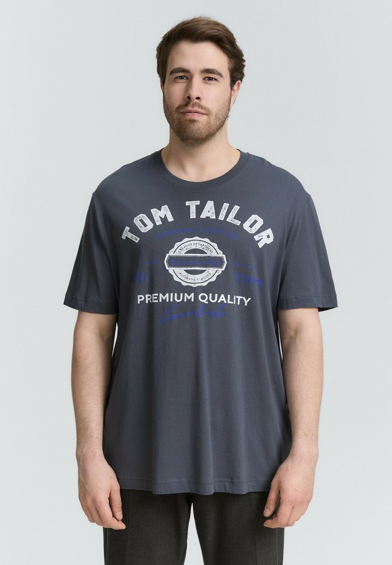 Czarna bawełniana koszulka z krótkim rękawem. Zawiera białe i niebieskie napisy, w tym "TOM TAILOR" i "PREMIUM QUALITY". Luźny krój.