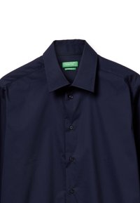 Camicia a maniche lunghe blu navy con colletto a punta, chiusura a bottoni e un'etichetta verde con la scritta "United Colors of Benetton". Texture liscia.