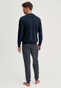 Marineblauw lange mouw shirt met ronde hals, gecombineerd met marineblauwe pyjamabroek met kleine witte stippen en elastische manchetten.