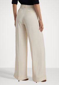 Beige wijde broek gemaakt van een soepele stof; heeft twee achterzakken en een op maat gemaakte tailleband. De zoom is licht uitlopend.