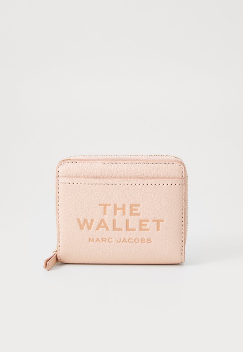 Rozā ādas maciņš ar reljefu uzrakstu "THE WALLET MARC JACOBS", kas aprīkots ar rāvējslēdzēju un kartīšu slots aizmugurē.