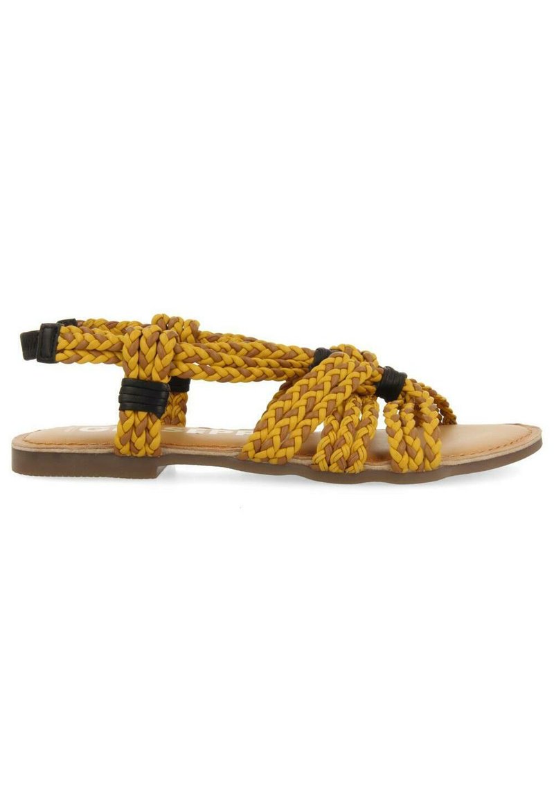 Sandalias trenzadas amarillas con acentos negros, suela plana, diseño abierto. Las correas texturizadas forman un patrón entrelazado sobre el pie.