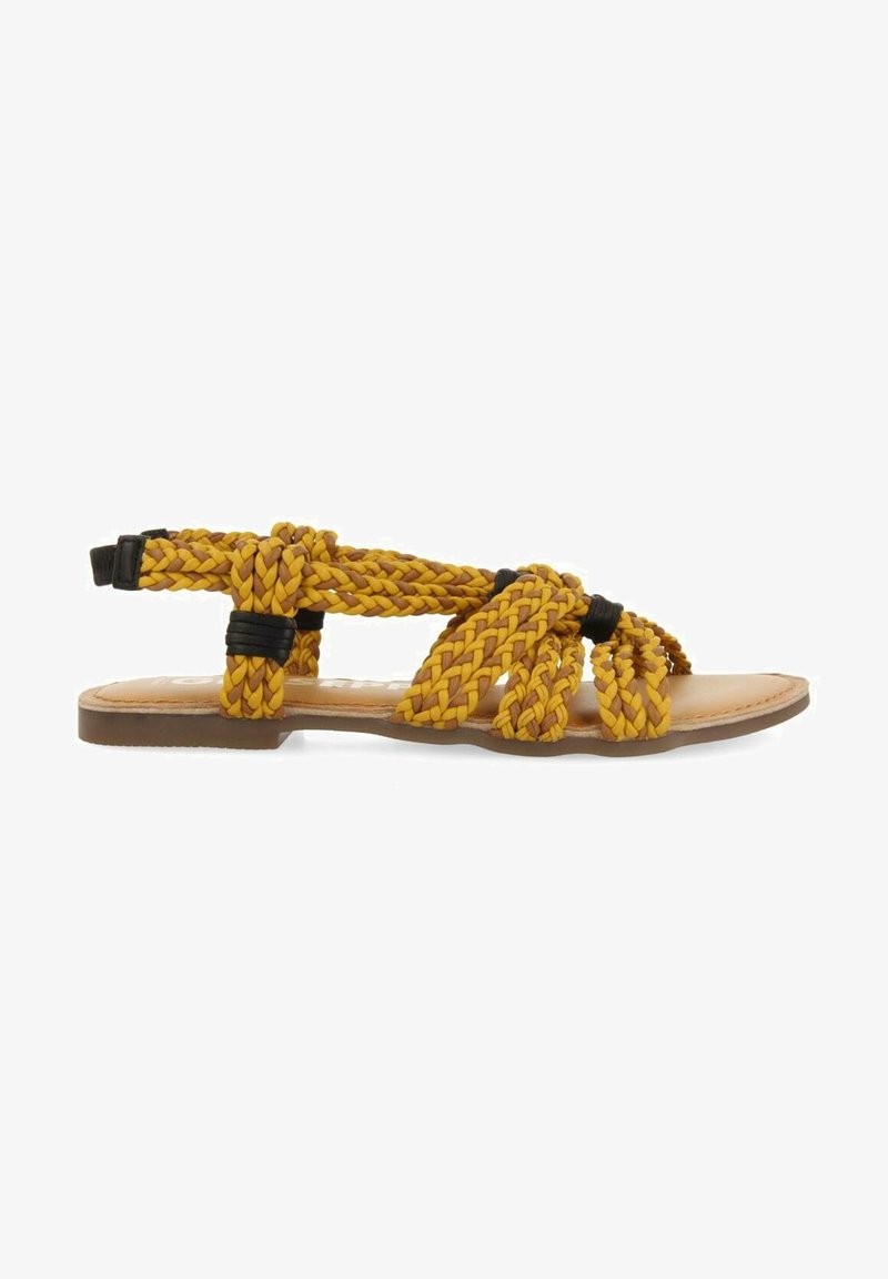 Sandales tressées jaunes avec des accents noirs, semelle plate, design ouvert. Les sangles texturées forment un motif tissé sur le pied.