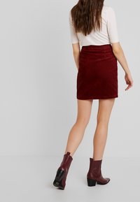 Burgundyröd kordflöjlsminikjol med vertikala ribbor, med en figurnära midja och bakfickor. Kombinerad med texturerade ankelskor.