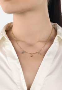Collar de cadena de oro con eslabones alargados, que presenta tres colgantes de piedras preciosas transparentes en diferentes formas colgando del centro.