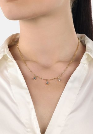 Collier en chaîne dorée avec des maillons allongés, comprenant trois pendentifs en pierres précieuses transparentes de formes variées suspendus au centre.