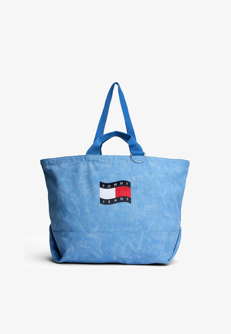 Light blue tote bag with dual handles and Tommy Jeans logo patch featuring black, white, and red color blocks on front center.
