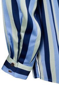 Manche de chemise à rayures verticales bleu clair, bleu marine et vert pâle, avec un poignet fixé par un bouton rond en métal.
