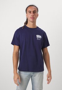 Navy blue cotton t-shirt with short sleeves, round neck, and a white graphic "1894" and text on the left chest area.