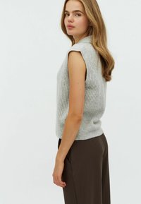 Top senza maniche a coste di un grigio chiaro, con scollatura a girocollo, caratterizzato da una vestibilità rilassata e una texture morbida, abbinato a pantaloni marroni.