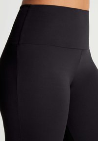 Vysoké černé legíny vyrobené z hladkého, pružného materiálu s elegantním designem a skrytými švy pro komfort a flexibilitu.