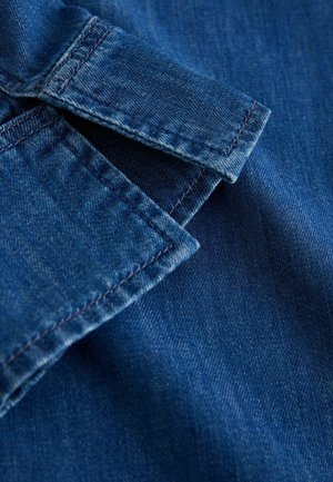 Denimikangas sügavsinise tooniga, millel on krõmpsuv kraa serv ja nähtavad õmbluste detailid, sile tekstuur ja kerge pleekimismuster.