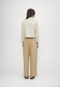 Lys beige croppet jakke med krage, kombinert med høytlivede, vide beige bukser. Glatt tekstur, rent design, minimale detaljer.