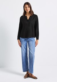 Maglietta nera a maniche lunghe con scollo a V e sottile placket, abbinata a jeans blu a vestibilità ampia e scarpe flat in stampa leopardata marrone.