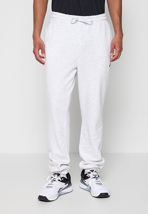 Man draagt lichtgrijze joggingbroek met elastische tailleband en witte sportschoenen tegen een effen achtergrond.