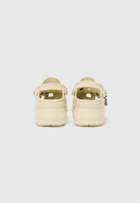 Crocs jaunes clairs avec un design à dos fermé, des trous de ventilation et des sangles ajustables. Logo visible sur le talon et le côté. Texture lisse.