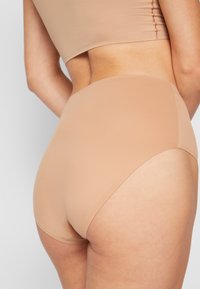 Beige hoge taille slip met een gladde stof, minimale naden en een subtiele glans, met een naadloos ontwerp voor comfort en een goede pasvorm.