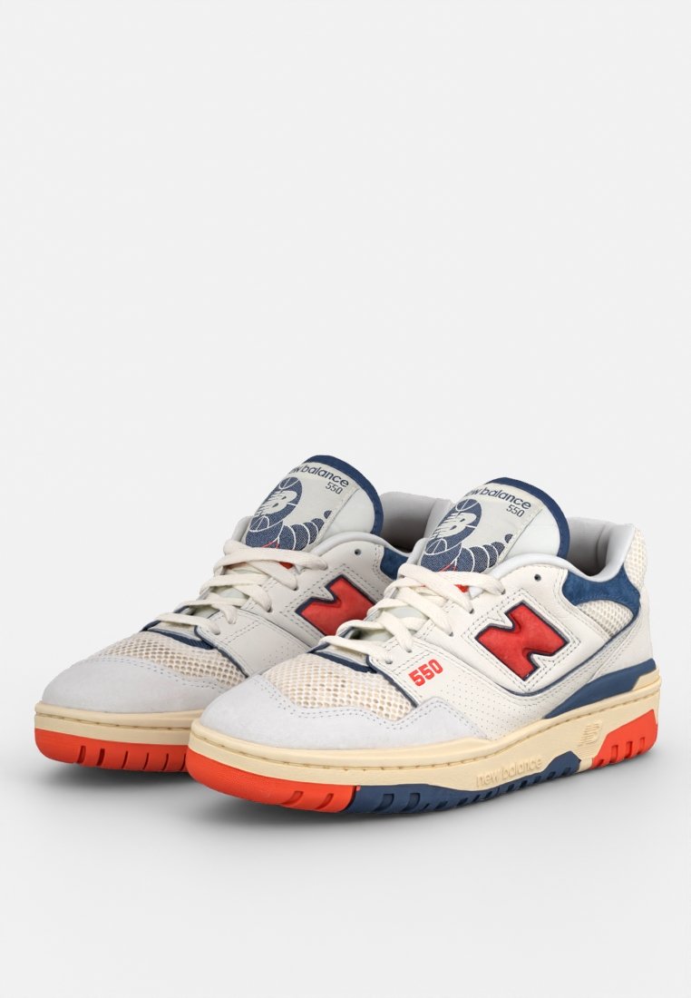 Weiße Netz- und Ledersneaker mit navyblauen und roten Akzenten, ausgestattet mit einem großen "N"-Logo, einem kreisförmigen Design an der Zunge und einer strukturierten Sohle.