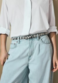 Jean taille haute bleu clair avec une coupe relax, associés à une ceinture noire et blanche à rayures avec une boucle ronde et une chemise blanche.